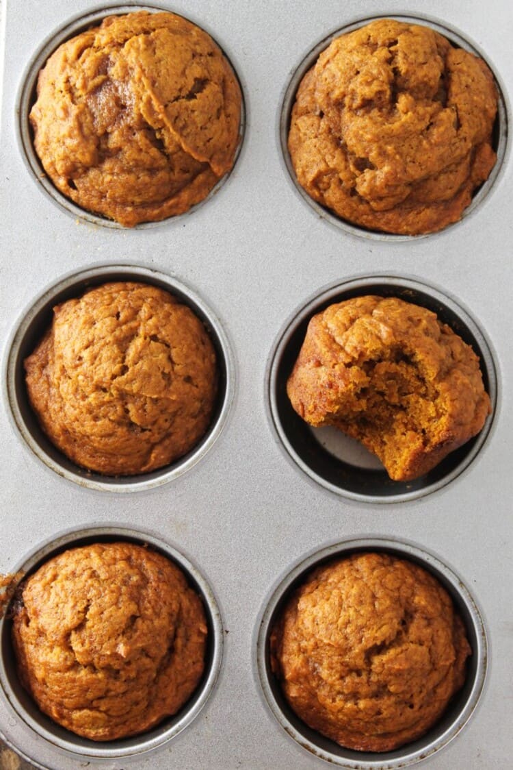 Six ready muffins in a baking tin with a bite on one muffin