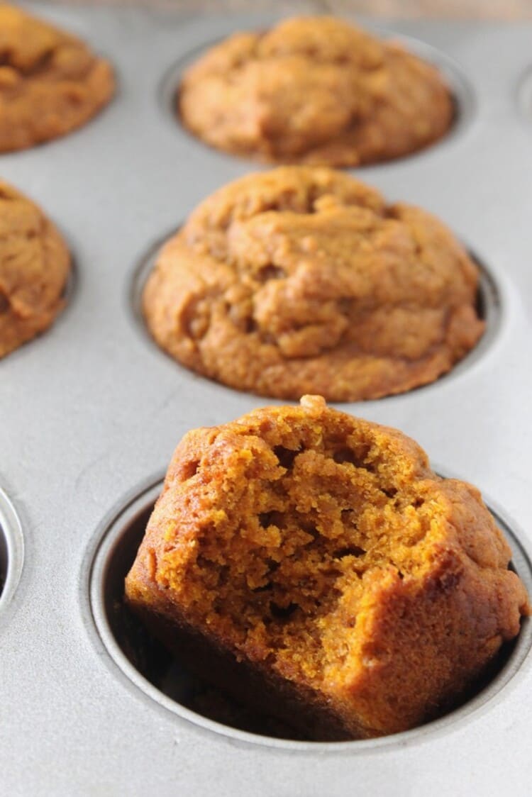 Close up photo of muffins in a baking tin with one with a bite 