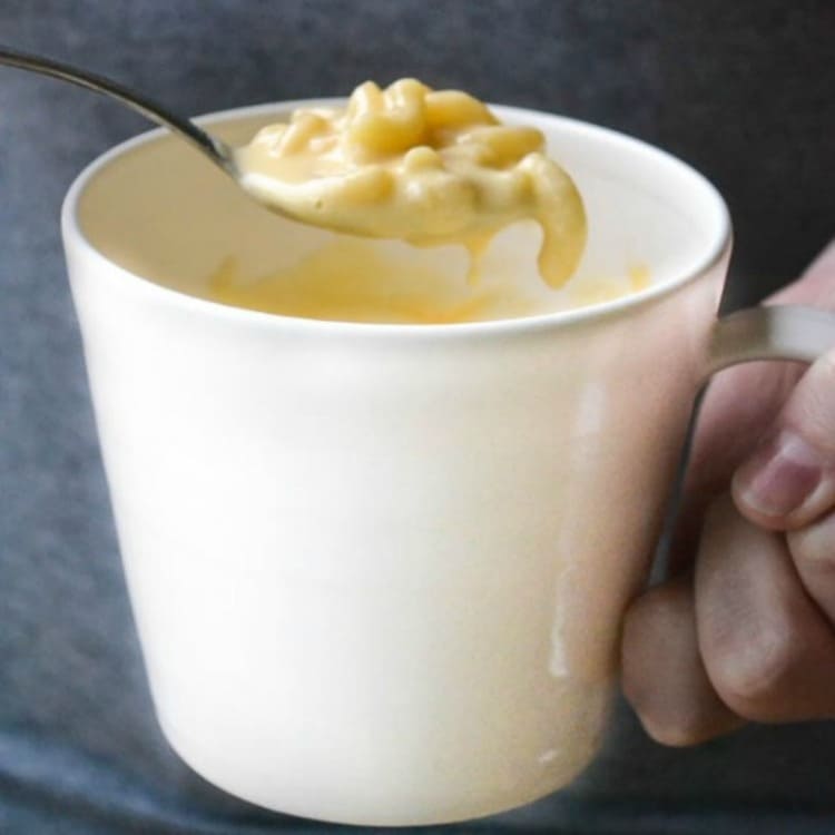 microwave mug snacks macaroni and cheese in a white cup and a hand holding it with a spoon