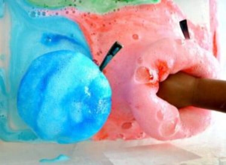 science project lemon suds eruptions colored in blue and pink and a hand touching it
