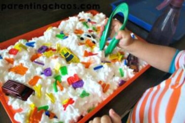 ABC Carwash sensory play - A photo of a child playing in a bin full of shaving cream and letters of the alphabet