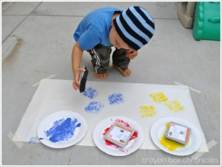 Creative sensory play - A child using carpet squares to paint on canvas on the floor