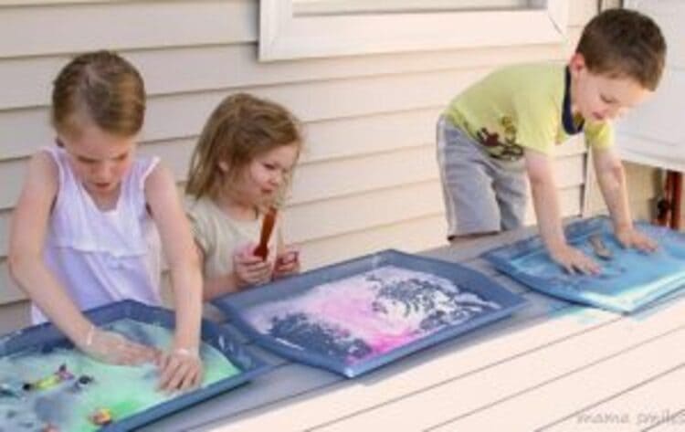 A photo of three children cornstarch painting on trays with their hands 