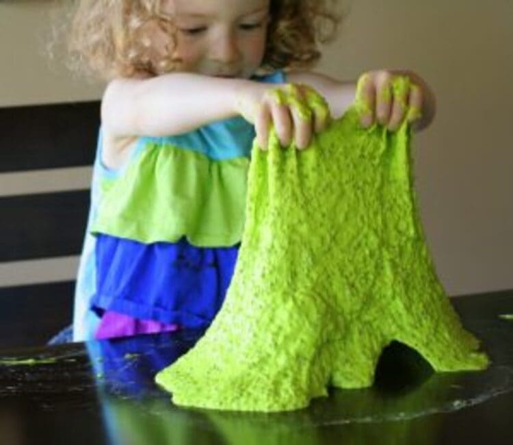 Edible slime sensory play - a photo of a little girl playing with edible slime, pulling it off the table