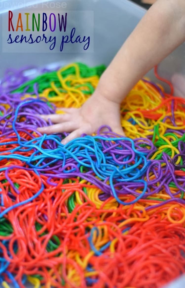 rainbow sensory play - a child's hand in a bin of rainbow colored noodles