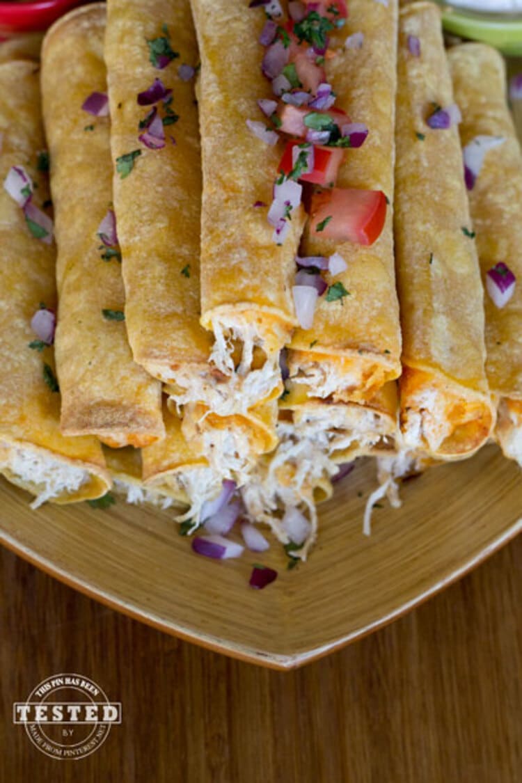 Crockpot Cream Cheese Taquitos - pyramid pile of creamy cheesy taquitos with salsa and onions on top