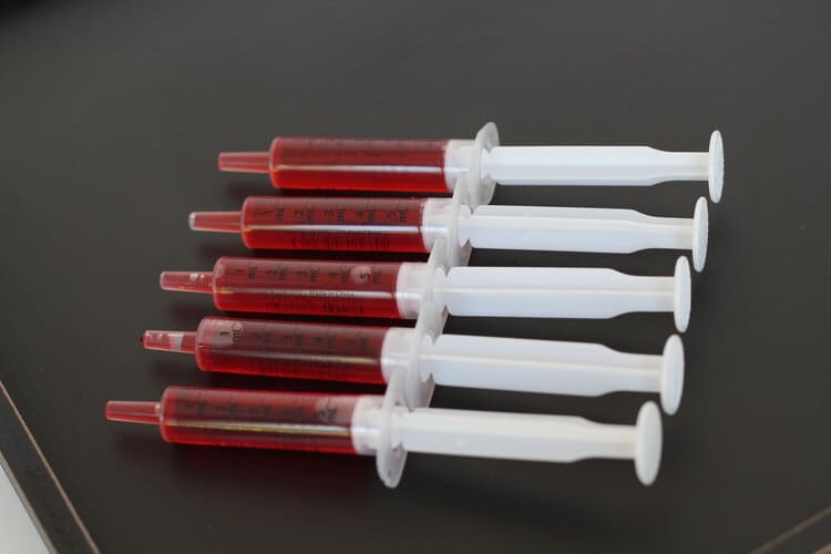 Up close photo of five syringes filled with grenadine syrup