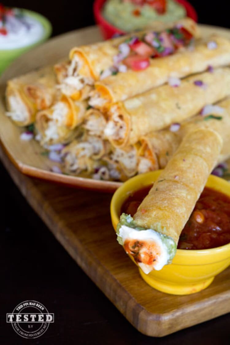 Crockpot Cream Cheese Taquitos - rolled corn tortillas with creamy cheese oozing out the ends, dripped over a red salsa cup