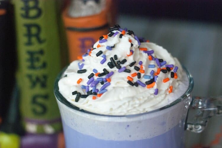 Purple colored hot cocoa treat with whip cream and Halloween sprinkles to die for