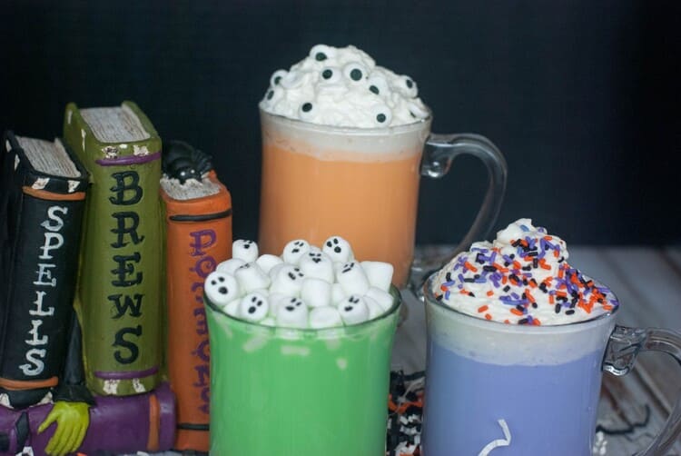 Spooky colored Halloween Hot Chocolate in darling mugs with festive treat toppings.