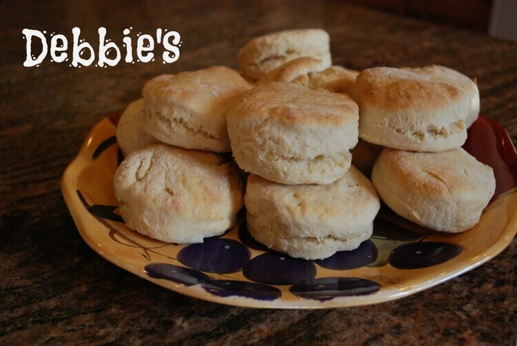 A large yellow plate with some black polka dot decorations placed on a dark grey marble work top with a stack of mile-high biscuits piled high, looking very appetising!