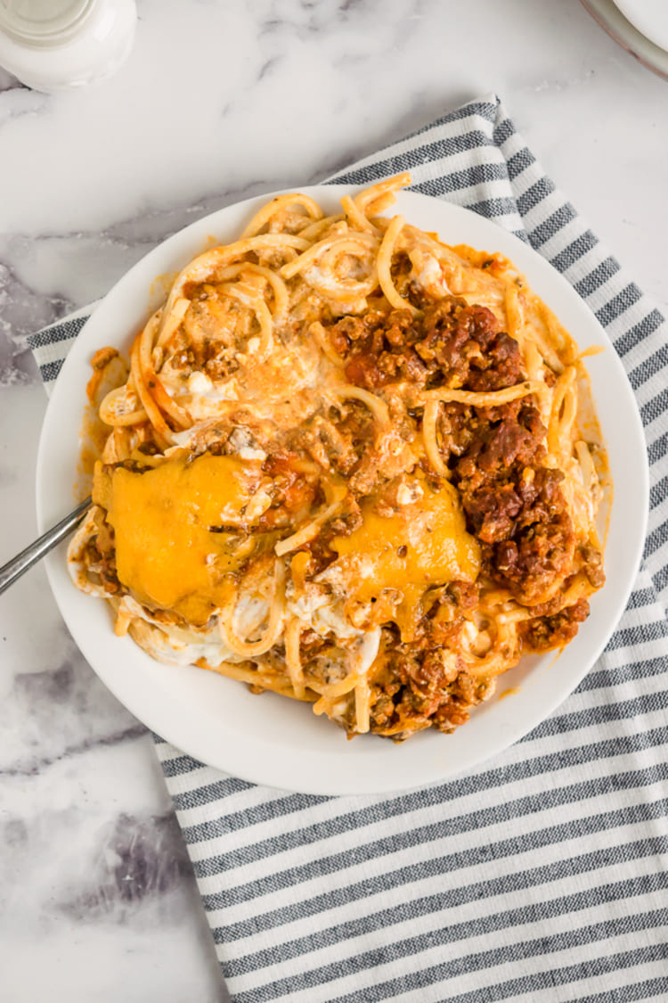 million dollar spaghetti meal in a white plate, a top view photo of a spaghetti meal on a grey and white kitchen towel on a white surface