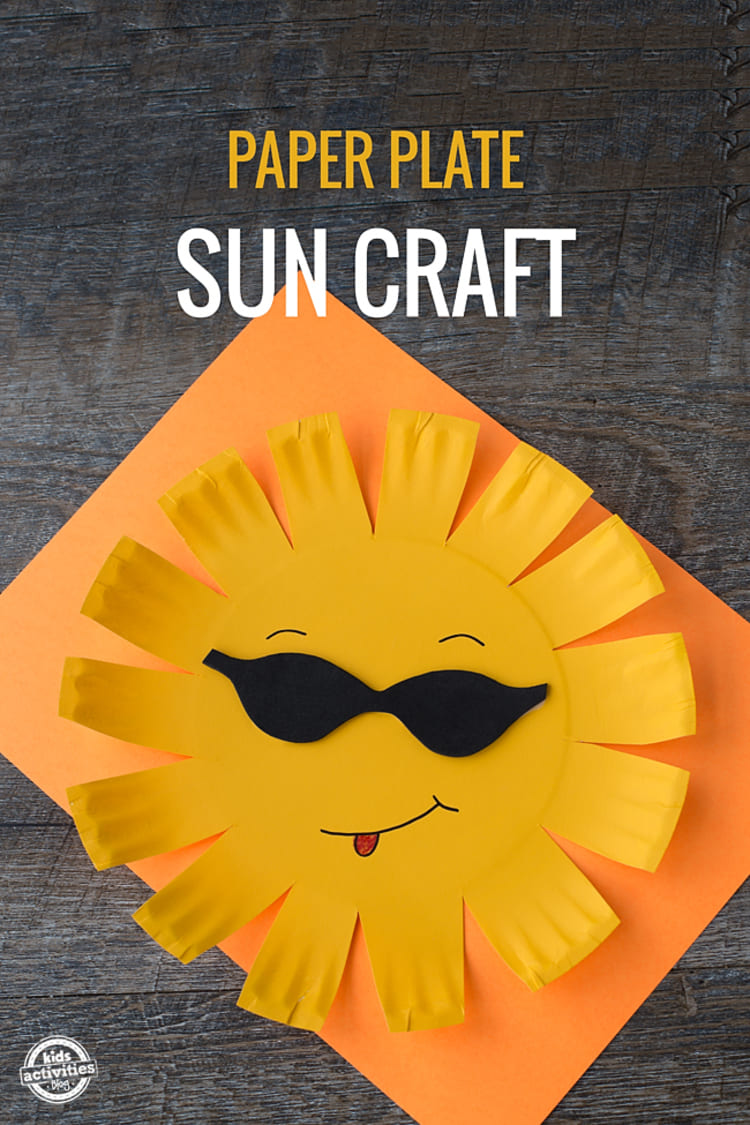 Paper plate craft yellow sun with black sunglassess smiling and showing tongue on a yellow paper sheet with black wooden background