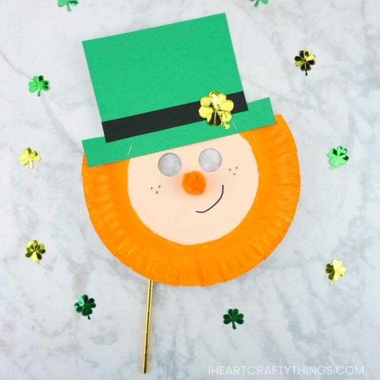 paper plate leprechaun mask with a green hat and an orange beard smiling on a marble background