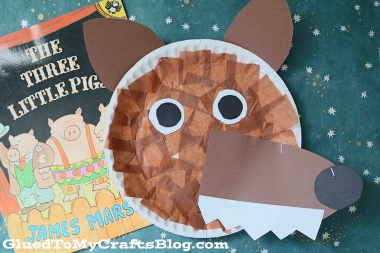 paper plate brown craft wolf on a green background next to the book The Three Little Pigs